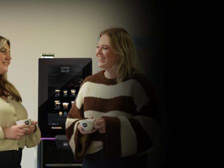 Twee leerkrachten genieten van koffie bij de koffiemachine op school